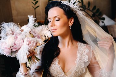 Gelin, şeffaf bir elbise ve iç çamaşırı içinde, elinde bir tüyle eski bir banyonun yanında oturuyor, gelinin sabahında..