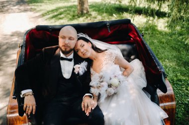 Gelin ve damat bir buketle doğada eski tarzda bir arabada oturuyorlar..