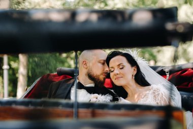Gelin ve damat bir buketle doğada eski tarzda bir arabada oturuyorlar..