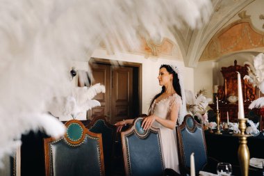 Masalarda tüylerle süslenmiş bir restoranın içinde gelinlik giymiş şık bir gelin..