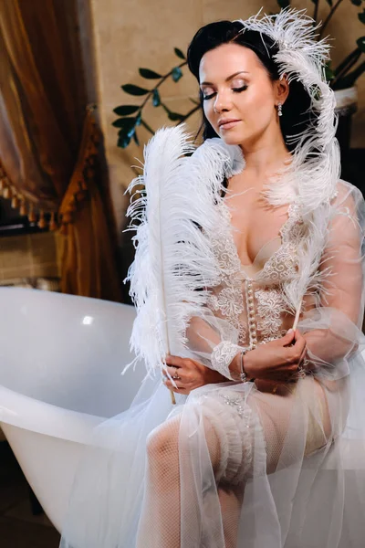 Gelin, şeffaf bir elbise ve iç çamaşırı giyip, eski bir küvete oturmuş, elinde bir tüyle, gelinin sabahında..