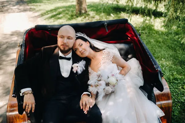 Gelin ve damat bir buketle doğada eski tarzda bir arabada oturuyorlar..