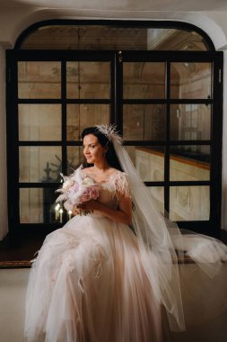 Gelinlik ve buket giymiş bir gelin açık eski bir pencerede oturur ve bakar..