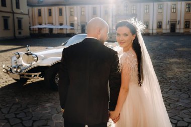 Şatonun avlusunda zarif bir çift eski bir arabanın yanında el ele yürür..