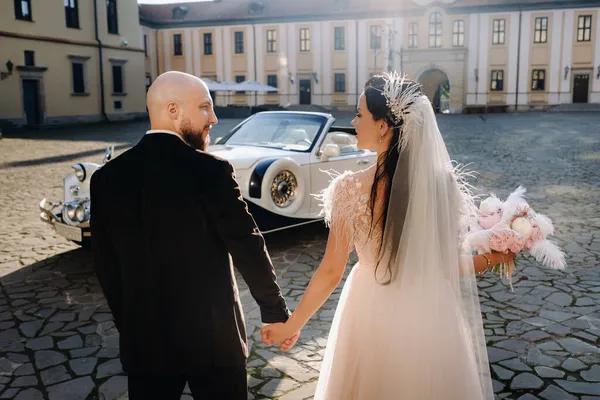 Şatonun avlusunda zarif bir çift eski bir arabanın yanında el ele yürür..