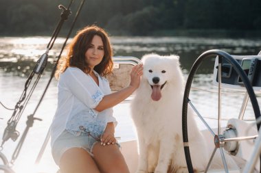 Denizde beyaz bir yatta büyük beyaz bir köpeği olan mutlu bir kadın..
