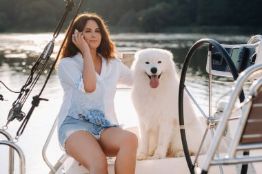 Denizde beyaz bir yatta büyük beyaz bir köpeği olan mutlu bir kadın..