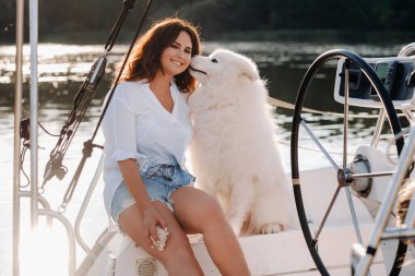 Denizdeki beyaz yatta büyük beyaz bir köpeği olan mutlu bir kadın. Köpek kulağıma fısıldıyor..