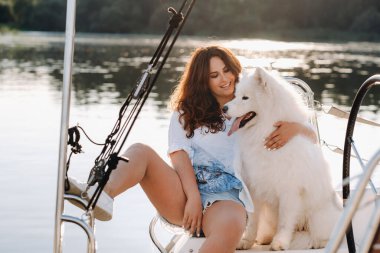 Denizde beyaz bir yatta büyük beyaz bir köpeği olan mutlu bir kadın..
