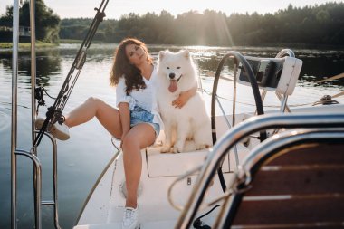Denizde beyaz bir yatta büyük beyaz bir köpeği olan mutlu bir kadın..