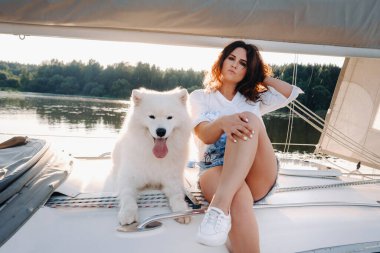 Denizde beyaz bir yatta büyük beyaz bir köpeği olan mutlu bir kadın..