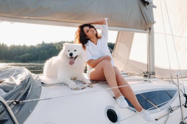 Denizde beyaz bir yatta büyük beyaz bir köpeği olan mutlu bir kadın..