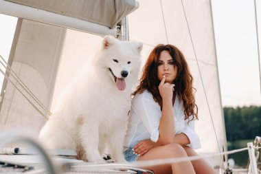 Denizde beyaz bir yatta büyük beyaz bir köpeği olan mutlu bir kadın..