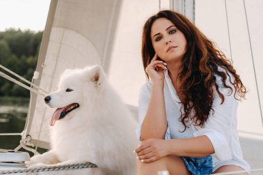 Denizde beyaz bir yatta büyük beyaz bir köpeği olan mutlu bir kadın..