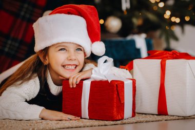 Noel Baba şapkalı mutlu küçük bir kız elinde hediyelerle gülümsüyor..