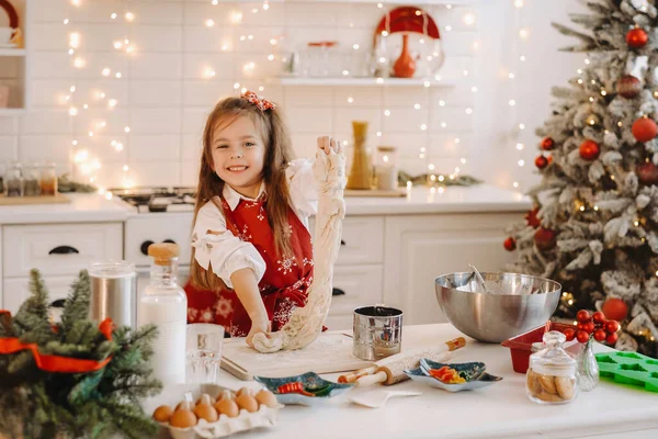 新年厨房里一个穿着红围裙的小女孩正在为圣诞饼干准备面团 — 图库照片