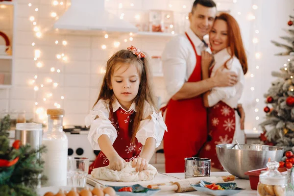 新年厨房里的一个小女孩做面团 妈妈和爸爸在她旁边看着她 — 图库照片