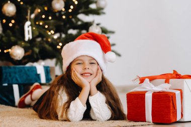 Noel Baba şapkalı mutlu küçük bir kız elinde hediyelerle gülümsüyor..