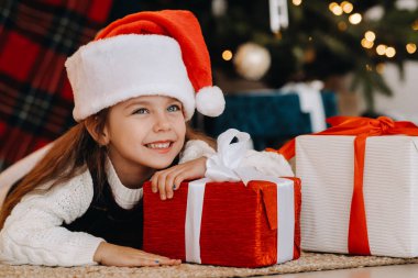 Noel Baba şapkalı mutlu küçük bir kız elinde hediyelerle gülümsüyor..
