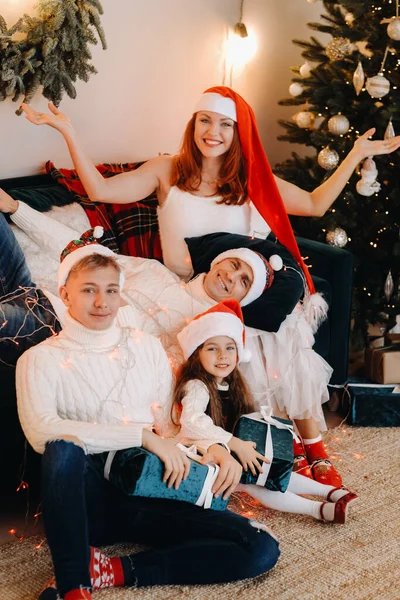 Retrato de cerca de una familia feliz sentada en un sofá cerca de un árbol de Navidad celebrando unas vacaciones —  Fotos de Stock