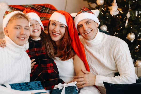Retrato de cerca de una familia feliz sentada en un sofá cerca de un árbol de Navidad celebrando unas vacaciones —  Fotos de Stock