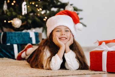 Noel Baba şapkalı mutlu küçük bir kız elinde hediyelerle gülümsüyor..