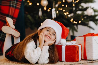 Noel Baba şapkalı mutlu küçük bir kız elinde hediyelerle gülümsüyor..