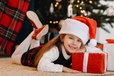 Noel Baba şapkalı mutlu küçük bir kız elinde hediyelerle gülümsüyor..
