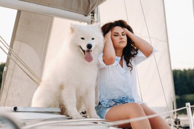 Denizde beyaz bir yatta büyük beyaz bir köpeği olan mutlu bir kadın..