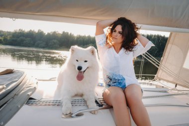 Denizde beyaz bir yatta büyük beyaz bir köpeği olan mutlu bir kadın..