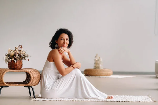 一个穿着亮晶晶内饰的白色太阳衣的女人坐在一块白色的地毯上 放松的概念 — 图库照片