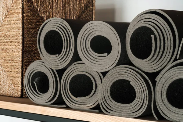 Gray yoga mats lying on a shelf, rolled up.