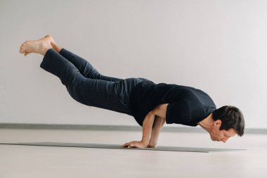 Siyah tişörtlü bir adam spor salonunda uzanıp esneme hareketleri yapıyor..