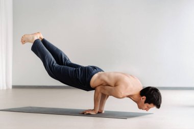 Çıplak gövdeli bir adam uzanmış spor salonunda esneme hareketleri yapıyor..