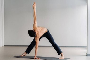 Çıplak gövdeli bir adam ayakta duruyor, spor salonunda esneme hareketleri yapıyor..