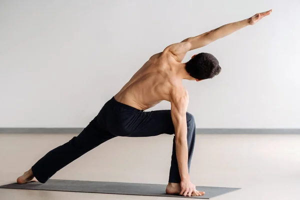 stock image A man with a bare torso trains standing up, doing stretching in the gym.