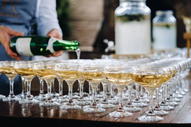 Barmen şarap bardaklarına şampanya ya da şarap dolduruyor açık hava düğün töreninde masada..