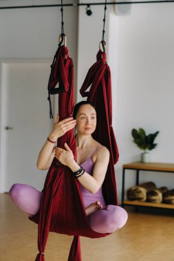 Kız sallanan bir hamakta oturuyor ve spor salonunda yoga yapıyor..