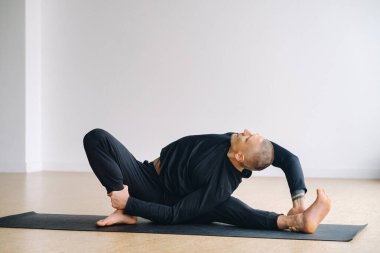 Siyah spor kıyafetli bir adam yoga yapıyor, spor salonunda esniyor..