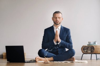 Resmi takım elbiseli bir adam spor salonunda dizüstü bilgisayarla meditasyon yapıyor..