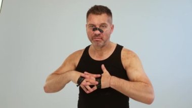 Siyah tişörtlü, uyuşturucu bağımlısı gibi görünen ve gri arka planda duran hırpalanmış bir adam.