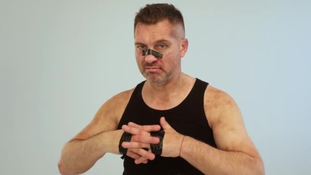 En misshandlad man i svart t-shirt som ser ut som en narkoman och ett fyllo står mot en grå bakgrund — Stockvideo