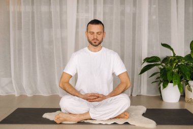Beyaz spor giyimli bir adam spor salonunda yoga yapıyor. Sağlıklı yaşam tarzı kavramı.