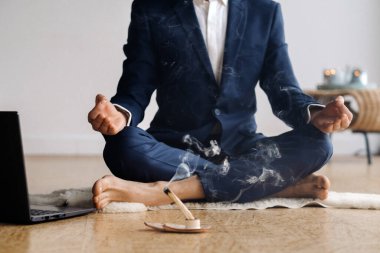 Resmi takım elbiseli bir adam spor salonunda dizüstü bilgisayarla meditasyon yapıyor..