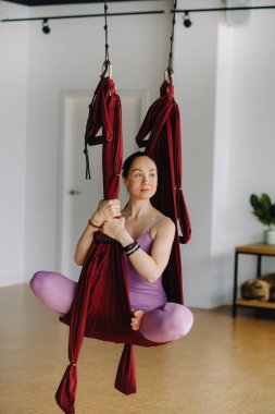 Kız sallanan bir hamakta oturuyor ve spor salonunda yoga yapıyor..