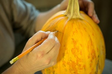 Jack O 'Lantern' i evde yapmak. Kalemle bir kadın eli, balkabağındaki kesik çizgilerini işaretler..