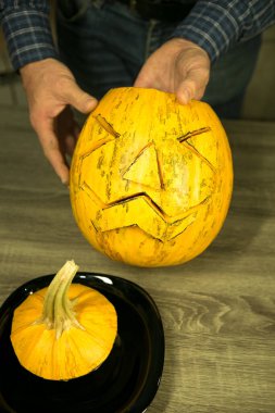 Jack O 'Lantern' i evde nasıl yaparım? Bıçaklı erkek eller, mutfak masasında kalan balkabağı artıkları. Seçici odak ve bokeh.
