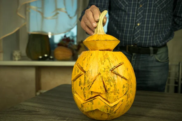 How to make Jack O\'Lantern at home? Male hands with knife, leftovers of pumpkin on the kitchen table. Selective focus and bokeh.