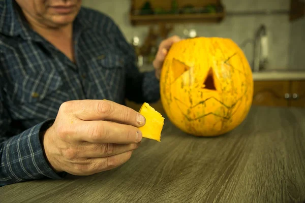 Halloween. How to make Jack O\'Lantern at home? Male hands with knife, leftovers of pumpkin on the kitchen table. Selective focus and bokeh.