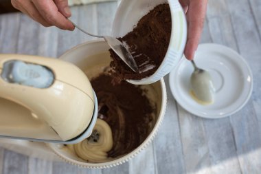 Adım adım ekşi çikolatalı pasta yapma süreci. Kadın elleri karıştırıcı kaseye kakao ekler. Pişirme kavramı.
